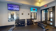 Located at 1028 E St Louis St in Springfield, Missouri, this fitness center offers a comprehensive and thoughtfully organized workout environment spread across a single floor. The space is designed with functionality in mind, featuring durable rubber flooring throughout that provides both safety and comfort during exercise.

The facility is divided into distinct workout zones. A dedicated free weights area houses multiple racks of dumbbells in varying sizes, accompanied by adjustable benches, making it ideal for strength training. Multiple wall-mounted flat-screen TVs are positioned throughout the space, keeping members entertained during their workouts.

The cardio section is well-appointed with a row of treadmills, elliptical machines, and stair climbers from reputable brands including Precor and Life Fitness. Cable machines and multi-station strength equipment are centrally positioned, offering a wide range of resistance training options.

The layout is open and airy, supported by multiple ceiling fans and recessed lighting that create a comfortable atmosphere. Large windows allow natural light to filter in and provide views of the surrounding exterior. Mirrored wall sections in select areas enhance the sense of space and assist with form during workouts. Glass-panel doors offer easy access throughout the facility, contributing to an organized and welcoming fitness environment.