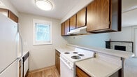Located at 210 E Lincoln Rd in Spokane, WA, this one-bedroom, one-bathroom unit offers a practical and efficiently designed single-floor layout. The kitchen is equipped with warm wood cabinetry, a white electric coil range, light countertops, and an under-cabinet range hood. A window with blinds allows natural light to brighten the space, while light-toned laminate flooring adds a clean, cohesive look throughout. A peninsula counter separates the kitchen from the living area, creating an open flow between the two spaces. The living area features neutral-toned carpet and connects seamlessly to the rest of the unit via a hallway with a louvered closet door. The bedroom is carpeted and features a wall-mounted air conditioning unit alongside a baseboard heater for year-round climate control, as well as a window overlooking greenery outside. The bathroom includes a tiled tub-shower combo with a grab bar, a toilet, and a wood-trimmed vanity with a single sink, medicine cabinet, and lighted mirror above. Textured ceilings are consistent throughout the unit. This residence offers a straightforward, functional design well-suited for those seeking a compact and manageable living space in Spokane.