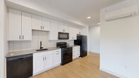 Located at 311 E Rio Grande St in Colorado Springs, CO, this thoughtfully designed one-bedroom, one-bathroom unit offers a clean, modern aesthetic across a single floor. The kitchen is a standout feature, showcasing crisp white shaker cabinets, a white subway tile backsplash, gray quartz-style countertops, and a full suite of black appliances including a refrigerator, electric range, microwave, and dishwasher. Light hardwood-style flooring runs throughout the main living areas, enhancing the bright, open feel of the space. The bedroom is carpeted for comfort and features corner windows that invite ample natural light, a ceiling fan, and a wall-mounted mini-split HVAC unit for efficient climate control. A stylish barn door connects the bedroom to the rest of the unit, adding a modern-industrial touch. The bathroom is well-appointed with white cabinetry, gray countertops, a tiled tub-shower combo with bold black tile accents, and a barn door entry. A dedicated laundry area includes a Whirlpool washer and built-in shelving for added storage. A closet provides additional organization space. The unit also features a balcony with open views of Colorado Springs' tree-lined neighborhood streets.