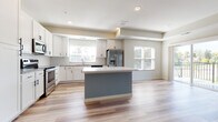This well-appointed single-floor residence showcases a clean, contemporary design throughout. The heart of the home is an open-concept kitchen and living area, where light wood-look flooring, crisp white shaker cabinetry, and a classic subway tile backsplash create a bright and inviting atmosphere. A central kitchen island with a white countertop provides additional prep and gathering space, while a full suite of stainless steel appliances — including a French door refrigerator, range, microwave, and dishwasher — delivers a fully equipped cooking environment. Multiple windows allow natural light to fill the open living space.

The bedrooms feature plush wall-to-wall carpeting and panel-style doors, offering a comfortable and quiet retreat. One bedroom includes a walk-in closet outfitted with wire shelving on multiple walls, providing generous storage capacity. A second closet with built-in shelving is also present in the bedroom wing.

The bathroom is finished with wood-look tile flooring, white cabinetry topped with granite counters, matte black hardware accents, and a dedicated shower stall. A dedicated laundry area accommodates a full-size washer and dryer with overhead shelving. The walk-in closet also features matching wood-look flooring, completing a cohesive and functional layout throughout the home.