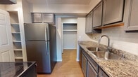 This single-floor, two-bedroom, two-bathroom residence offers a well-organized layout designed for comfortable everyday living. The kitchen is a standout feature, outfitted with gray shaker-style cabinetry, granite-look countertops, a tile backsplash, stainless steel appliances including a refrigerator, dishwasher, and electric range, and a double basin sink. A dedicated pantry closet provides ample storage directly off the kitchen. Wood-style flooring runs through the kitchen and connects to the dining area, which is highlighted by a modern sputnik chandelier.

The living room is generously sized with plush carpeting, a corner fireplace as a focal point, and a sliding glass door that opens to a private balcony with outdoor views. Both bedrooms feature soft carpet flooring and good natural light; one bedroom includes a walk-in closet. Each bathroom is finished with gray cabinetry, a white countertop vanity, chrome fixtures, and wood-style flooring. A dedicated in-unit laundry area with a full-size washer and dryer and overhead shelving adds practical convenience to this well-appointed residence.