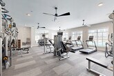 Located at 200 Travis Dr in McDonough, GA, this modern fitness center offers a comprehensive, single-floor exercise facility designed to support a full range of workout routines. The space is divided into distinct functional zones, seamlessly connected for an efficient and comfortable workout experience.

The main exercise floor is finished with durable, multi-toned carpet tile and is outfitted with an extensive selection of strength training equipment, including cable machines, a power rack with weight storage, adjustable benches, and a dedicated free weights area with a full-length mirror wall. Multiple ceiling fans mounted overhead provide continuous air circulation throughout the space.

A row of treadmills and cardio machines lines one wall, positioned alongside large windows with horizontal blinds that allow natural light to filter in while offering views of the outdoor pool area. The bright, neutral color palette of the walls and the recessed lighting contribute to an open and energizing atmosphere.

A secondary area with light hardwood flooring serves as a flexible studio or stretching zone, equipped with a wall-mounted television and additional windows overlooking the surrounding community and greenery. This versatile space is well suited for functional training, with battle ropes and sled equipment also present. Together, the zones create a well-rounded, amenity-rich fitness facility.
