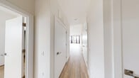 This well-designed single-floor residence offers a thoughtfully organized layout comprising two bedrooms, two bathrooms, a combined kitchen and living area, and a dedicated closet. Light wood-tone flooring runs consistently throughout the unit, lending a cohesive, contemporary aesthetic to every room.

The open-concept kitchen and living area serves as the heart of the home. The kitchen is outfitted with flat-front wood-grain cabinetry extending to the ceiling, stainless steel appliances including a gas range, microwave, and French door refrigerator, a white subway tile backsplash, and a large central island with a quartz countertop illuminated by geometric gold pendant lights. The adjacent living area features large sliding glass doors and windows that introduce generous natural light and outdoor views.

A bright hallway with multiple white panel doors connects the private quarters. The spacious primary bedroom includes sliding glass door access to an outdoor space and an en-suite bathroom featuring a floor-to-ceiling marble-tiled walk-in shower with a rainfall showerhead and frameless glass enclosure. The secondary bedroom is well-proportioned with a window providing natural light. Both bedrooms feature the same warm wood flooring found throughout the residence.