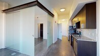 This single-floor space showcases a thoughtfully designed contemporary layout that balances open living with defined functional zones. The interior is anchored by polished concrete flooring throughout the main living areas, lending an industrial-modern aesthetic that pairs well with the clean white walls and neutral palette.

A standout architectural feature is the frosted glass sliding partition system, mounted on a dark metal track, which elegantly separates the sleeping area from the main living space. This design allows natural light to filter through while maintaining privacy, and opens fully to create a more expansive feel.

The galley-style kitchen is well-appointed with dark espresso cabinetry, granite countertops, a white subway tile backsplash, and a full suite of stainless steel appliances including a refrigerator, range, microwave, and dishwasher. A secondary kitchen configuration visible in additional images mirrors this setup with similar finishes.

The bedroom area features rich dark hardwood flooring and a series of tall, dark-framed windows that frame broad city and skyline views, flooding the room with natural light. A walk-in closet with dark wood shelving provides generous storage.

The bathroom is finished with neutral tile throughout, including a soaking tub with tiled surround, complemented by dark cabinetry. Overall, the space presents a cohesive modern urban aesthetic.