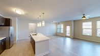 Located at 1421 Legacy Falls Dr in Wake Forest, NC, this well-appointed one-bedroom, one-bathroom residence offers a thoughtfully designed single-floor layout with a comfortable sense of space throughout. The open-concept kitchen and living area serves as the heart of the home, anchored by a large center island with a white quartz-style countertop, an undermount sink, and elegant pendant lighting overhead. Dark espresso cabinetry reaches toward the ceiling, providing ample storage, while stainless steel appliances—including a refrigerator with ice maker, range, and microwave—complete the modern kitchen. Light wood-style flooring flows seamlessly through the main living and dining areas, complementing the neutral warm-toned walls. The living room is bathed in natural light from multiple windows fitted with horizontal blinds, and a door opens directly to a private outdoor patio, offering convenient outdoor access. The bedroom features plush carpeting, a ceiling fan with lighting, and dual windows that frame outdoor views. A generously sized walk-in closet with wire shelving and hanging rods provides practical storage. The bathroom is finished with a dark wood vanity, light countertop, an undermount sink, and a full soaking tub and shower combination with tile surround. A hallway connects all areas of this clean, modern residence.