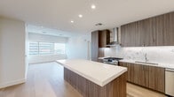 This contemporary residence offers five bedrooms and one bathroom across a single, thoughtfully designed floor. The open-concept kitchen serves as a central highlight, showcasing rich wood-grain cabinetry, a striking marble-look backsplash, a stainless steel range with a statement hood vent, and a large waterfall-edge island with a crisp white countertop — ideal for both cooking and entertaining. The kitchen flows seamlessly into the living area, which is bathed in natural light from large windows framing impressive city skyline views. Light-toned hardwood flooring extends throughout the main living areas, lending warmth and cohesion to the space. The bedrooms are generously proportioned, with the primary bedroom featuring expansive floor-to-ceiling windows that capture sweeping urban vistas. Secondary bedrooms are finished with neutral carpeting, offering comfort and versatility. The bathroom features marble-style tile flooring, a floating wood vanity, and clean, minimalist fixtures. A dedicated laundry room houses a stacked washer and dryer unit for added convenience. Two closets, including a spacious walk-in with full-length hanging rails, provide ample storage. Recessed lighting throughout maintains a clean, modern aesthetic across the entire residence.