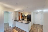 Located at 10051 109 St NW in downtown Edmonton, this 2-bedroom, 1-bathroom unit offers a well-designed layout that maximizes its compact footprint. Rich hardwood-style flooring flows throughout, adding warmth and visual continuity across every room.

The open-concept kitchen is a standout feature, anchored by a peninsula with a dark countertop and double stainless steel sink. White cabinetry lines the walls, complemented by a tile backsplash, black appliances, a bold burnt-orange accent wall, and pendant lighting that adds a modern touch. Built-in open shelving provides additional storage and display space.

The kitchen flows seamlessly into the living area, which benefits from natural light through a window framing views of the surrounding Edmonton cityscape. The hallway connects the living space to the private sleeping quarters.

The primary bedroom is a comfortable size, featuring a window with urban views, a double-door closet, and an adjacent walk-in closet for generous storage. The second bedroom also enjoys natural light and hardwood-style flooring. In total, the unit offers four closets, ensuring ample storage throughout.

The bathroom features a corner glass-enclosed shower, a vessel sink atop a white vanity with a dark countertop, a large mirror with shelving, and a striking orange accent wall that ties back to the kitchen's design palette.