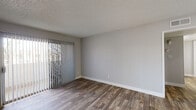 This single-floor unit presents a clean, modern aesthetic throughout, highlighted by wood-look flooring and neutral gray walls that create a cohesive and contemporary feel. The open layout connects key living areas, as visible in the floor plan, with a clear flow between the living space, kitchen, and bedrooms.

The living area is generously sized, featuring a sliding glass door with vertical blinds that allows natural light to fill the room while providing access to an outdoor area. A secondary entrance door is also present in this space. Textured ceilings are consistent throughout the unit.

The kitchen is well-appointed with white shaker-style cabinetry, granite-look countertops, and a full suite of stainless steel appliances including a gas range, microwave, refrigerator, and dishwasher. A ceiling fan provides additional ventilation, and wood-look flooring continues seamlessly into this space. A peninsula with a sink adds functional counter space.

The bedrooms are comfortably proportioned, each featuring wood-look flooring, neutral walls, white baseboards, and windows with blinds that bring in natural light and views of surrounding greenery.