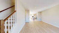 This newly constructed, three-floor home showcases a bright and modern design with a cohesive, neutral color palette and light hardwood flooring that flows seamlessly throughout. The open-concept main level draws the eye toward a well-appointed kitchen, where light wood cabinetry, a classic white subway tile backsplash, and gleaming quartz countertops set a clean, contemporary tone. A generously sized center island with pendant lighting serves as the kitchen's focal point, complemented by stainless steel appliances and recessed lighting overhead. A sliding glass door off the kitchen provides direct access to an outdoor area, allowing natural light to fill the space. A staircase with warm wood treads and a white baluster railing connects all three levels, adding an elegant architectural element to the interior. The upper floors feature spacious bedrooms with ample closet space, including a walk-in closet with built-in shelving, offering excellent storage solutions. A full bathroom presents a sliding glass-enclosed shower with tile surround, a wood-toned vanity, and crisp white countertops. Throughout the home, recessed lighting, clean white trim, and neutral wall tones create a bright, welcoming ambiance suited to a variety of living arrangements.