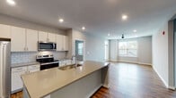 This well-appointed single-floor unit offers a thoughtfully designed open-concept layout that seamlessly connects the kitchen, dining, and living areas. The kitchen is a standout feature, equipped with stainless steel appliances including a French door refrigerator, electric range, and built-in microwave. White shaker-style cabinetry, a classic subway tile backsplash, and light quartz countertops complement the central island, which includes an undermount sink and additional prep space. Rich, warm-toned hardwood flooring flows throughout the main living areas, adding depth and character to the space. The spacious living room benefits from natural light through large windows and is finished with a ceiling fan overhead. Bedrooms are carpeted for comfort, each featuring multiple windows with blinds and ceiling fans, creating bright and airy retreats. Two full bathrooms serve the unit — one with a walk-in glass-door shower and a vanity with quartz counters, the other with a shower-tub combination, both finished with the same warm hardwood flooring and neutral grey wall tones. Recessed lighting throughout the unit provides consistent, modern illumination, while the clean, neutral color palette lends a fresh and contemporary ambiance to the entire space.