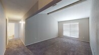 This single-story residence offers a practical and comfortable layout designed for everyday living. The kitchen is configured as a galley-style space, featuring dark cabinetry with sleek hardware, granite-style countertops, a double stainless steel sink, and black appliances including a refrigerator, stove, microwave, and dishwasher. Hardwood-style flooring runs through the kitchen, which opens toward the living area via a pass-through counter, creating a connected, functional flow between the two spaces.

The living room is highlighted by a ceiling fan with a light fixture, a fireplace with a white mantel, and a window fitted with horizontal blinds that allows natural light to filter in. Plush carpeting adds warmth to this gathering space. An adjacent bedroom features vaulted ceilings with an angled roofline, a large window, and soft carpet underfoot, contributing to a notably airy atmosphere. Another bedroom includes a built-in shelving and desk unit along with a ceiling fan, providing useful storage and workspace. The bathroom is finished with hardwood-style flooring, clean white fixtures, and a straightforward, functional design. A hallway connects the rooms, transitioning between carpet and hardwood-style surfaces throughout.