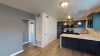 This single-floor unit offers a thoughtfully updated interior with a cohesive, modern aesthetic throughout. The open-concept kitchen is a standout feature, showcasing dark navy cabinetry, striking marble-look quartz countertops, a tile backsplash, and a peninsula that adds both workspace and a casual dining option. Pendant lighting illuminates the kitchen, which is equipped with stainless and black appliances including a refrigerator, electric range, microwave, and dishwasher. Natural light filters in through window blinds above the sink.

The living area features warm wood-look laminate flooring, soft blue-gray accent walls, and a ceiling fan with light fixture. A large window with horizontal blinds brings in ample natural light, while a sliding glass door in an adjacent room opens directly to the private outdoor patio. This exterior space features low-maintenance artificial turf, gravel edging, and a horizontal-slat wood privacy fence, creating a calm outdoor retreat.

The bedrooms carry the same cool-toned color palette and wood-look flooring. Bathrooms include one with full marble-look tile surrounding a tub-shower combo with sliding glass doors, and another with a walk-in glass-enclosed shower finished in warm beige stone-look tile with mosaic tile flooring. Together, these spaces deliver a clean, updated living environment.