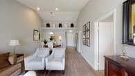Located at 5770 NW 74th Pl in Coconut Creek, Florida, this single-story home presents a well-designed interior with a cohesive, neutral color palette throughout. The living area is notably spacious, featuring vaulted ceilings that enhance the sense of openness, wood-look flooring, and recessed lighting. A decorative display shelf positioned near the ceiling adds architectural interest to the space. The living room accommodates generous seating and connects seamlessly to the dining area, which is highlighted by a pendant light fixture above a round dining table and a pass-through window offering a direct view into the kitchen.

The kitchen is well-appointed with white cabinetry, light countertops, stainless steel appliances including a refrigerator, range, microwave, and dishwasher, and a mosaic tile backsplash that adds a coastal-inspired accent. A mirrored backsplash element further brightens the space.

The bedroom features carpeted flooring for comfort, an en-suite bathroom access, and ample space. The bathroom is finished with white cabinetry, a vanity with a large mirror, and wood-look flooring. A sliding glass door in the living area provides natural light and access to an outdoor space.