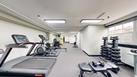 Located at 8818 Blairwood Rd in Nottingham, MD, this fitness center offers a comprehensive workout facility designed to accommodate a wide range of exercise needs. The space is organized across a single floor and is divided into functional zones that flow seamlessly from one area to the next.

The main workout floor features a strong selection of cardio equipment, including treadmills, stationary bikes, an elliptical trainer, and a rowing machine. Adjacent to the cardio zone is a dedicated strength training area equipped with a multi-function cable machine, a weight bench, and a well-stocked dumbbell rack offering a full range of free weights. A collection of medicine balls and exercise balls adds to the functional training options available.

The interior is finished with neutral-toned walls and carpeted flooring throughout, contributing to a clean and professional atmosphere. Large recessed panel lighting ensures the space is consistently and evenly illuminated. A full-length wall mirror in the free weights area enhances the sense of openness while allowing users to monitor their form. A wall-mounted air conditioning unit provides climate control for year-round comfort. The layout is thoughtfully arranged to maximize usable floor space while maintaining clear pathways between equipment stations, making the facility practical and accessible for all users.
