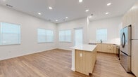 This well-appointed 2-bedroom, 2-bathroom single-story residence offers a thoughtfully designed layout with modern finishes throughout. The open-concept kitchen and living area serves as the heart of the home, featuring light wood cabinetry, a white quartz-topped island, stainless steel appliances including a refrigerator and microwave, recessed lighting, and warm wood-look flooring. Multiple windows flood the space with natural light, creating a bright and airy atmosphere. A glass door provides additional access to the exterior. A hallway connects the living areas to the private quarters, where both bedrooms are finished with plush carpet and large windows fitted with roller shades. The primary bedroom includes a walk-in closet with built-in shelving. The bathrooms feature wood-look tile flooring, white tile surrounds, and matte black fixtures, including a glass-enclosed walk-in shower. A dedicated laundry room houses a full-size front-loading Samsung washer and dryer with overhead shelving for added storage. Two closets provide generous storage throughout. The consistent use of white walls, matte black hardware, and warm wood-tone flooring gives the entire residence a cohesive, clean, and contemporary aesthetic.