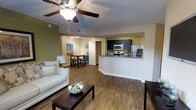 This 3-bedroom, 2-bathroom single-story residence offers a well-designed open-concept floor plan that maximizes functionality and flow. The living area features warm wood-style flooring, a ceiling fan with integrated lighting, and a textured ceiling, creating a comfortable and inviting atmosphere. An accent wall painted in earthy green adds a distinct visual element to the living space.

The living room transitions naturally into a dedicated dining area, which accommodates a bar-height table with stools, ideal for casual meals. Track lighting overhead provides focused illumination for the space. Adjacent to the dining area, the kitchen is equipped with dark cabinetry, stainless steel appliances including a microwave and range, and a tiled backsplash that adds texture and contrast. A peninsula counter separates the kitchen from the main living area, offering additional workspace and a natural boundary between zones.

The open layout connects all shared living spaces cohesively, allowing for easy movement throughout. The consistent wood-style flooring runs throughout the main living areas, contributing to a unified and polished aesthetic. Overall, the residence offers a practical and well-appointed living environment suited for everyday comfort.