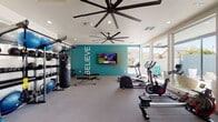 This fitness center is a thoughtfully designed single-level space that combines functionality with an energizing aesthetic. The room is anchored by a bold teal accent wall featuring a prominent "BELIEVE" motivational inscription in white lettering, complemented by a wall-mounted flat-screen television. Full-length mirrors along one wall amplify the sense of space and support proper form during workouts.

The cardio zone is well-appointed with treadmills, elliptical trainers, stationary bikes, a rowing machine, and a stair climber. A dedicated strength training area includes a full dumbbell rack, adjustable weight benches, a heavy punching bag, a cable functional trainer, and TRX suspension straps for versatile resistance training. Exercise and stability balls are neatly stored on a wall-mounted rack.

Large floor-to-ceiling windows line one wall, flooding the space with natural light and offering direct views of an outdoor pool area. Oversized ceiling fans with wide-span blades provide effective air circulation throughout the room. The neutral carpet flooring and recessed lighting contribute to a clean, modern finish. The overall atmosphere is motivating and well-organized, catering to a broad range of fitness needs.