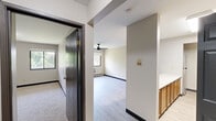 This 2-bedroom, 2-bathroom residence is thoughtfully laid out across a single floor, offering a practical and comfortable living arrangement. The living room serves as the central gathering space, featuring light gray hardwood-style flooring, a ceiling fan, large windows that bring in natural light and outdoor greenery views, and a wall-mounted HVAC unit for climate control. Adjacent to the living room, the kitchen is well-equipped with warm oak cabinetry — both upper and lower — white countertops, a double-basin sink, an electric range, and a refrigerator. A peninsula counter adds additional workspace and visual separation between the kitchen and the rest of the unit. Both bedrooms are carpeted and feature windows overlooking lush outdoor scenery, with baseboard heating along the walls. The primary bedroom offers a generous footprint, while the second bedroom is equally well-proportioned. Each room is served by a dedicated closet for ample storage. The two bathrooms are clean and functional — one features a wood-toned vanity with a mirrored medicine cabinet and a tub/shower combination, while the second offers a white vanity and an open tub/shower. Light vinyl flooring runs throughout the bathrooms and kitchen, while the hallway connects all rooms efficiently.