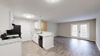 Located at 1213 Edenham Ct in Chesapeake, Virginia, this well-appointed 2-bedroom, 2-bathroom single-story home offers a thoughtfully designed layout with modern finishes throughout. The open-concept kitchen and living area serves as the heart of the home, featuring white shaker-style cabinetry, granite-look countertops, a black undermount sink, and black appliances including a refrigerator, electric range, and dishwasher. Wood-look plank flooring runs throughout the main living spaces, adding warmth and continuity to the design. The living room is bright and welcoming, highlighted by French doors that invite natural light and provide outdoor access. The two bedrooms are carpeted for comfort, with neutral tones and textured ceilings. The primary bedroom includes a sliding double-door closet and a window with outdoor views. Both bathrooms are finished with white vanities and a tub-shower combination accented by matte black fixtures. A hallway connects the private areas of the home, fitted with panel-style doors and matte black hardware for a cohesive, contemporary aesthetic. Textured ceilings are present throughout, and the overall color palette of soft beige and white creates a clean, move-in-ready atmosphere.