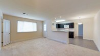 This single-floor space showcases an open-concept design that seamlessly connects the living area to the kitchen. The living area is finished with plush, neutral-toned carpeting, creating a comfortable and cohesive feel throughout. A large window along one wall allows natural light to fill the space, brightening the warm beige walls and contributing to an airy atmosphere. A white-paneled exterior door nearby adds a secondary source of natural light.

The kitchen is defined by striking dark cabinetry that contrasts sharply against the light walls and white appliances, including a built-in microwave and a range. A peninsula with a light-toned countertop serves as a natural divider between the kitchen and living area, offering additional workspace and potential seating. Recessed lighting and a skylight above the kitchen ensure the workspace remains well-lit. The kitchen floor transitions to a hard surface, providing a practical distinction from the carpeted living space. A hallway visible beyond the kitchen suggests additional rooms within the unit, further enhancing the functional layout of this well-designed space.