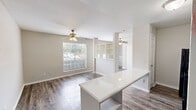 This single-floor unit offers a thoughtfully arranged open-concept layout that maximizes every inch of its compact footprint. The living area features durable hardwood-style flooring, neutral beige walls, and a textured ceiling, creating a clean and cohesive aesthetic. A ceiling fan with a light fixture keeps the space comfortable, while a large window with blinds fills the room with natural light and offers views of the surrounding greenery. Built-in open shelving adds both functionality and a subtle architectural detail to the shared living and kitchen space.

The kitchen is designed for efficiency, equipped with black appliances including an electric range with overhead ventilation and a dishwasher, complemented by white cabinetry and light stone-look countertops. A prominent kitchen island with built-in lower shelving provides additional prep space and storage, serving as a natural divider between the kitchen and living area. A dedicated entry door with a security lock offers direct access from the exterior.

The bathroom includes a full tub-and-shower combo with white tile surround and brushed nickel fixtures, maintaining the unit's clean, functional design. Throughout the space, consistent flooring and a neutral color palette create a unified, move-in-ready environment.
