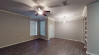 This single-story space offers a well-designed layout with consistent finishes throughout. The main living area is generously sized, featuring dark hardwood-style flooring, crown molding, and neutral gray walls that create a clean, modern aesthetic. Two windows positioned at a corner angle allow natural light to filter in, complemented by a ceiling fan with integrated lighting and a decorative pendant light. A door provides direct exterior access from this space.

The entryway area mirrors the living space in style, with the same dark flooring, crown molding, and a ceiling fan overhead. A brick-patterned entry mat marks the front door, adding a subtle decorative touch at the threshold.

The galley-style kitchen is efficiently organized with dark espresso cabinetry lining both walls, granite-patterned countertops, and a white subway tile backsplash. It includes a stainless steel double sink, electric range, and built-in microwave. Double doors open to an adjacent utility or storage area.

The bedroom features plush carpeting, neutral walls, and a ceiling fan, offering a comfortable and quiet retreat. The bathroom includes wood-style flooring, a full tub-shower combination with white tile surround, and dark cabinetry for storage.