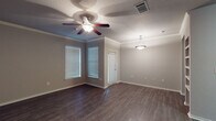 This single-story space offers a well-designed layout with consistent finishes throughout. The main living area is generously sized, featuring dark hardwood-style flooring, crown molding, and neutral gray walls that create a clean, modern aesthetic. Two windows positioned at a corner angle allow natural light to filter in, complemented by a ceiling fan with integrated lighting and a decorative pendant light. A door provides direct exterior access from this space.

The entryway area mirrors the living space in style, with the same dark flooring, crown molding, and a ceiling fan overhead. A brick-patterned entry mat marks the front door, adding a subtle decorative touch at the threshold.

The galley-style kitchen is efficiently organized with dark espresso cabinetry lining both walls, granite-patterned countertops, and a white subway tile backsplash. It includes a stainless steel double sink, electric range, and built-in microwave. Double doors open to an adjacent utility or storage area.

The bedroom features plush carpeting, neutral walls, and a ceiling fan, offering a comfortable and quiet retreat. The bathroom includes wood-style flooring, a full tub-shower combination with white tile surround, and dark cabinetry for storage.