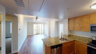 This single-floor residence offers a thoughtfully designed open-concept layout that seamlessly connects the kitchen and living area. The living room is highlighted by rich hardwood flooring, crown molding, track lighting, and a sliding glass door that opens to a private balcony, filling the space with natural light and outdoor views. The kitchen is well-equipped with warm honey-toned cabinetry, granite countertops, stainless steel appliances including an electric range with an over-the-range microwave, a dishwasher, and a peninsula with a sink that doubles as a breakfast bar — ideal for both cooking and casual dining. A stacked washer and dryer unit is conveniently housed within the unit, adding everyday practicality. The bedroom features plush carpeting, crown molding, and a generously sized window with vertical blinds that allow for adjustable natural light. Two bathrooms serve the residence: one features a soaking tub and shower combination with tile surround, while the second offers a granite-topped vanity with warm wood cabinetry, tile flooring, and a large framed mirror. Both bathrooms are equipped with grab bars, reflecting accessible design. The overall ambiance is clean, bright, and move-in ready.