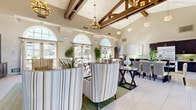 Located at 4914 Olive St in Montclair, California, this single-floor community space combines architectural elegance with modern functionality. The interior is defined by dramatically vaulted ceilings adorned with rich, dark-stained exposed wood beams, creating a grand sense of openness and volume throughout. Large arched windows and French doors line the walls, flooding the space with abundant natural light while offering views of the surrounding outdoor environment.

The main lounge area features refined furnishings, including striped high-back accent chairs, a plush sofa, and round side tables, centered around a built-in entertainment unit with shelving, a fireplace, and a flat-screen television. Elegant chandelier and pendant lighting fixtures complement the warm, neutral color palette of cream and beige tones offset by dark wood accents.

The full kitchen is outfitted with dark espresso cabinetry, stainless steel appliances including a refrigerator and wall oven, green glass tile backsplash, and light countertops. A generous central island with a gas cooktop provides ample workspace and casual seating. The adjacent dining area accommodates multiple guests across both formal dining tables and a long communal bar-height counter. Light tile flooring flows seamlessly throughout, tying together the open, airy, and welcoming ambiance of the entire space.