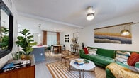 This thoughtfully designed multi-floor residence spans three levels, offering a diverse range of living spaces connected by a central staircase. The open-plan living area is warm and inviting, featuring light wood-style flooring, a textured ceiling, and large windows that usher in natural light. A tiled fireplace anchors one end of the living room, complemented by sliding glass doors that open to a private outdoor area with views of surrounding greenery. The adjacent dining space is defined by elegant floor-length curtains framing bright windows, creating an intimate yet airy atmosphere. The kitchen is well-appointed with two-tone cabinetry — white uppers and grey lowers — stainless steel appliances, a grey tile backsplash, and generous counter space, all set on light wood-style flooring. Bedrooms are carpeted for comfort and include ample natural light through slatted blinds; at least one bedroom benefits from direct access to a full bathroom featuring a soaking tub and shower combination. Additional storage is available via a utility closet with built-in shelving. Throughout the residence, the design balances practical functionality with a lively, eclectic aesthetic that makes each room feel distinct and purposefully arranged.