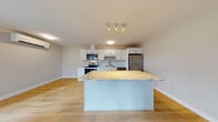 Located at 171 Scarborough Downs Road in Scarborough, Maine, this single-floor unit offers a well-designed, open-concept layout with modern finishes throughout. The kitchen serves as a central focal point, featuring crisp white shaker-style cabinetry, light marble-patterned countertops, a full suite of stainless steel appliances including a range, microwave, refrigerator, and dishwasher, and a central island with an overhang ideal for casual seating. Light hardwood-style flooring flows seamlessly through the kitchen and living areas, lending a bright, cohesive feel to the open floor plan. The spacious living area benefits from natural light and a clean, neutral color palette that enhances the sense of openness. The bedrooms are carpeted for comfort and feature large windows that frame views of the surrounding landscape, with baseboard heating units along the walls. The full bathroom is finished with a white vanity with ample cabinetry, a tub-shower combination, brushed nickel fixtures, and hardwood-style flooring, maintaining the unit's consistent modern aesthetic. The overall ambiance is clean, bright, and move-in ready, reflecting contemporary residential design suited to the Scarborough, Maine setting.