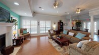 Located at 2500 Frederick Rd in Claremore, Oklahoma, this single-floor facility offers a thoughtfully designed and inviting interior that balances functional workspaces with comfortable communal areas. The space is anchored by striking white decorative columns with detailed capitals that frame the open floor plan, lending a classic architectural character throughout.

The expansive lounge area serves as the heart of the space, featuring rich hardwood flooring, tray ceilings with crown molding, and multiple ceiling fans with recessed lighting. A fireplace with a white mantle serves as the focal point of the lounge, flanked by large windows with plantation shutters that allow generous natural light to fill the room. The seating area is arranged around a wood coffee table atop a patterned area rug, creating a warm and welcoming atmosphere. A bold teal accent wall adds a vibrant, distinctive touch to the lounge.

Adjacent to the lounge is a professional workspace with dark wood desks and upholstered seating, ideal for meetings or administrative tasks. Framed credentials and decorative artwork adorn the walls. French doors lead to an exterior entrance, enhancing accessibility and natural light in this area.

A compact kitchenette provides everyday convenience, outfitted with white cabinetry, a coffee station, and a sink — accented by the same vivid teal backsplash wall seen throughout the space, tying the design together cohesively.