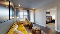 This well-appointed single-floor residence showcases a thoughtfully designed open-concept layout with a seamless flow between the kitchen, dining, and living areas. The kitchen is a standout feature, equipped with stainless steel appliances, a full suite of light wood-grain cabinetry, a dark subway tile backsplash, and a central white island that serves as both a prep space and a casual gathering point. Pendant lighting adds a refined touch overhead, while rich dark hardwood flooring ties the space together.

The living area exudes warmth and personality, with teal-painted accent walls, large windows that invite natural light, and access to an outdoor balcony. The entry nook includes a built-in bench with shelving, providing convenient storage.

The primary bedroom features plush carpeting, a ceiling fan, and an en-suite bathroom, offering a comfortable private retreat. A second bedroom is equally well-lit, with large windows and soft carpeting. The bathroom includes a soaking tub surrounded by glossy dark subway tile, complementing the modern aesthetic found throughout the residence.

Overall, the space combines contemporary design elements with warm, eclectic touches, creating a vibrant and functional living environment.