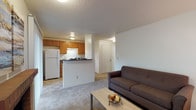 This single-floor unit offers a practical and comfortable layout, thoughtfully designed to maximize functionality across its key living areas. The open-concept living room and kitchen form the heart of the space, with plush carpeting underfoot in the lounge area and tile flooring in the kitchen. The living room provides ample space for a sofa and coffee table, with a textured ceiling overhead and neutral walls throughout. A half-wall peninsula separates the living area from the kitchen, which is outfitted with warm wood-toned cabinetry, dark countertops, a coil-burner electric range, a refrigerator, and a dishwasher. A sliding glass door in the kitchen opens to an outdoor area, filling the space with natural light and views of a green exterior. The bedroom is a serene retreat, featuring soft carpet, a large window with a view of surrounding trees, and a mirrored sliding-door closet that enhances the sense of space. The full bathroom includes a tub-shower combination, a vanity with wood cabinetry, dark countertops, and tile flooring. The overall ambiance is clean, neutral, and move-in ready.
