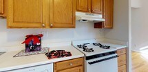 Located at 88 Clinton Pl in Hackensack, New Jersey, this single-floor unit offers a well-organized layout with clean, neutral interiors throughout. Warm hardwood floors extend across the living areas and bedrooms, reflecting natural light and lending a welcoming character to each room.

The living spaces are bright and open, with large windows dressed in horizontal blinds that frame views of the surrounding neighborhood's mature trees. Radiator heating units beneath the windows ensure year-round comfort. The rooms feature crisp white walls and multiple doorways that connect the layout efficiently, with closet space visible in at least one of the bedrooms.

The kitchen is equipped with warm oak cabinetry providing generous storage, white countertops, a gas range, a dishwasher, and an overhead ventilation hood — offering a practical and functional cooking environment.

The full bathroom is finished with white tile wainscoting and features a tub-shower combination with a sliding glass door, a single-sink vanity with a mirrored medicine cabinet, and a small window for natural ventilation.

The unit's entry area flows seamlessly into the main living space, maintaining an open and airy feel. Overall, this unit presents a tidy, move-in-ready space with classic finishes and functional amenities in a residential Hackensack location.