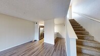 Located at 5505 Springhouse Dr in Pleasanton, CA, this two-story residence is thoughtfully laid out across two well-proportioned floors. The main level hosts an open-concept kitchen and living area, where warm wood-look flooring flows seamlessly throughout. The kitchen features dark espresso cabinetry, stainless steel appliances including a refrigerator, microwave, and range, complemented by a light quartz countertop with a built-in sink and pendant lighting overhead. A textured ceiling adds character to the space, while a sliding glass door floods the living area with natural light and provides direct access to an outdoor patio. A carpeted staircase with clean white railings connects the two floors. The upper level continues the cohesive design with additional wood-look flooring and soaring vaulted ceilings that create an airy, open atmosphere. A second sliding glass door leads to a balcony, extending the living space outdoors. The upper floor also includes a full bathroom with a tub-shower combination, dark vanity cabinetry, and wood-look flooring, as well as a spacious walk-in closet outfitted with wire shelving and carpet flooring for added comfort.