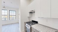Located at 118–126 S 10th St in Newark, NJ, this efficiently designed unit offers a thoughtfully arranged single-floor layout comprising a kitchen and a full bathroom. Light wood-style luxury vinyl flooring runs throughout the main living area and kitchen, lending a clean, cohesive aesthetic to the space.

The kitchen is well-appointed with stainless steel appliances, including a gas range with a range hood, a refrigerator, and a double-basin sink. Wood-toned lower cabinetry pairs with crisp white upper cabinets and a classic subway tile backsplash, while granite countertops provide a polished, durable work surface. Recessed lighting illuminates the kitchen efficiently.

The main living area benefits from two large, grid-pane windows fitted with black frames that flood the room with natural light and offer views of the surrounding Newark neighborhood. A pendant light fixture adds a stylish focal point to the bright, open space, complemented by clean white walls and tall baseboards.

The bathroom features a refined tile design, with large-format light gray wall tiles accented by wood-toned vertical tile detailing. The floor incorporates a striking mix of gray and wood-look tiles in a horizontal pattern. Black matte hardware and fixtures add a modern contrast, completing a bathroom that is both functional and visually appealing.