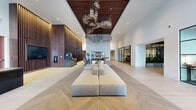 Located at 1140 Bannock Street in Denver's vibrant arts district, this residential lobby makes a powerful first impression with its expansive, single-floor layout spanning a substantial footprint. Upon entry, wide-format stone tile floors transition into a striking light wood herringbone pattern that flows throughout the main hall. Soaring double-height ceilings amplify the sense of grandeur, while an oversized sculptural chandelier crafted from organic, branch-like elements anchors the central space dramatically overhead. A partial wood-slat ceiling inset adds warmth and architectural contrast to the white walls above.

The main lounge area features modular upholstered seating arranged around a full-height stone fireplace, creating an inviting focal point. Adjacent to the seating area, a concierge desk is framed by a lush, full-scale living moss wall — a bold biophilic design statement that introduces vibrant natural color. Warm wood slatted wall panels and backlit open shelving line the surrounding walls, contributing a refined, contemporary aesthetic.

A dedicated mailroom features wood-paneled ceilings, a central round dining table with mid-century modern chairs, globe pendant lighting, and floor-to-ceiling resident mailboxes. The entry vestibule showcases textured stone cladding and black-framed glass doors, setting the tone for the elegant interior beyond.
