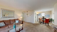 This Cambridge Apartments unit offers a thoughtfully designed single-floor layout that balances comfort and functionality. The open-concept living and dining area is generously proportioned, featuring plush wall-to-wall carpeting and warm, neutral-toned walls that create a welcoming atmosphere. The living room accommodates ample seating and is accented by a decorative mirror, while the adjacent dining area is anchored by a round glass-top table beneath an elegant chandelier, making it ideal for entertaining.

The galley-style kitchen is efficiently laid out with white cabinetry, laminate countertops, a double sink, and white appliances, all set on easy-care wood-look flooring. A warm accent wall adds a touch of character to the space.

The bedrooms are carpeted and bright, benefiting from natural light through window blinds. The primary bedroom features a walk-in closet, providing generous storage. Both bathrooms are finished with wood-look flooring, white vanities, and tub-shower combinations — one with classic tile surround — offering clean, functional spaces.

Throughout the unit, the consistent use of neutral tones, soft carpeting, and warm lighting creates a cohesive and comfortable living environment well-suited for everyday living.