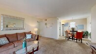 This Cambridge Apartments unit offers a thoughtfully designed single-floor layout that balances comfort and functionality. The open-concept living and dining area is generously proportioned, featuring plush wall-to-wall carpeting and warm, neutral-toned walls that create a welcoming atmosphere. The living room accommodates ample seating and is accented by a decorative mirror, while the adjacent dining area is anchored by a round glass-top table beneath an elegant chandelier, making it ideal for entertaining.

The galley-style kitchen is efficiently laid out with white cabinetry, laminate countertops, a double sink, and white appliances, all set on easy-care wood-look flooring. A warm accent wall adds a touch of character to the space.

The bedrooms are carpeted and bright, benefiting from natural light through window blinds. The primary bedroom features a walk-in closet, providing generous storage. Both bathrooms are finished with wood-look flooring, white vanities, and tub-shower combinations — one with classic tile surround — offering clean, functional spaces.

Throughout the unit, the consistent use of neutral tones, soft carpeting, and warm lighting creates a cohesive and comfortable living environment well-suited for everyday living.