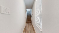 This two-story home offers a thoughtfully designed layout spread across two floors, combining modern finishes with practical living spaces. The main level features an open-concept kitchen and living area, where light wood-look flooring flows seamlessly throughout. The kitchen is a standout, equipped with stainless steel appliances including a refrigerator, range, and microwave, complemented by granite countertops, a central island, and light-toned shaker-style cabinetry. The living area receives natural light through windows fitted with white horizontal blinds, and a front entry door with glass panel adds additional brightness. A staircase with warm wood-toned treads and a sleek railing connects the two floors, framed by crisp white walls and a window that draws in natural light. Upstairs, the generous primary bedroom includes access to a dedicated walk-in closet with full rod storage and an en suite bathroom featuring a single-sink vanity with light wood cabinetry, white countertops, and a glass-enclosed shower. Two additional bedrooms offer comfortable proportions and share access to well-appointed bathrooms. A dedicated laundry room houses a full-size washer and dryer. Wood-look flooring is consistent throughout, tying together the clean, contemporary aesthetic of the entire home.