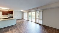 This first-floor apartment at 705 Monroe St in Rockville, Maryland offers a well-designed single-level layout with consistent wood-style flooring throughout. The kitchen is a functional galley-style space featuring rich dark wood cabinetry, granite countertops, stainless steel appliances including a refrigerator and dishwasher, and a stainless steel sink — providing a clean, modern aesthetic. The living area is bright and open, highlighted by large sliding glass doors fitted with vertical blinds that provide direct access to an outdoor green space and allow abundant natural light to flow in. The layout also includes bedrooms with ample wall space, closet access, and windows that bring in additional natural light. One bedroom features soft green-toned walls and a full closet with panel doors, while another offers neutral tones and a window with exterior views. The bathroom is well-appointed with a full soaking tub and shower combo with white tile surround, a dark wood vanity with storage, a framed mirror, and chrome fixtures. Throughout the unit, neutral wall colors and dark wood-tone flooring create a cohesive and practical living environment. The unit's ground-floor location with outdoor access adds a notable layer of convenience and livability.