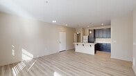 This single-floor, 2-bedroom, 2-bathroom residence is thoughtfully designed to maximize functionality and comfort. The open living area serves as the heart of the unit, finished with light-toned hardwood-style flooring that runs throughout the main spaces. Large windows and a glass exterior door bathe the room in natural light while providing access to an outdoor balcony area, creating a bright and airy ambiance. A wall-unit HVAC system ensures year-round climate control.

The kitchen is a standout feature, showcasing dark espresso cabinetry that extends to the ceiling for ample storage, contrasted by crisp white quartz countertops. A central island with a built-in sink adds both prep space and a casual dining option, while stainless steel appliances—including a refrigerator, electric range, and built-in microwave—complete the modern aesthetic.

Both bedrooms are carpeted for warmth and comfort. The primary bedroom includes a spacious walk-in closet fitted with wire shelving and hanging rods. The second bedroom features a sliding-door closet with dedicated hanging storage. A hallway bathroom and a second bathroom near the laundry area—which houses a full-size washer and dryer—provide added convenience. Neutral tones and clean finishes throughout lend the space a cohesive, contemporary character.
