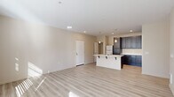 This single-floor, 2-bedroom, 2-bathroom residence is thoughtfully designed to maximize functionality and comfort. The open living area serves as the heart of the unit, finished with light-toned hardwood-style flooring that runs throughout the main spaces. Large windows and a glass exterior door bathe the room in natural light while providing access to an outdoor balcony area, creating a bright and airy ambiance. A wall-unit HVAC system ensures year-round climate control.

The kitchen is a standout feature, showcasing dark espresso cabinetry that extends to the ceiling for ample storage, contrasted by crisp white quartz countertops. A central island with a built-in sink adds both prep space and a casual dining option, while stainless steel appliances—including a refrigerator, electric range, and built-in microwave—complete the modern aesthetic.

Both bedrooms are carpeted for warmth and comfort. The primary bedroom includes a spacious walk-in closet fitted with wire shelving and hanging rods. The second bedroom features a sliding-door closet with dedicated hanging storage. A hallway bathroom and a second bathroom near the laundry area—which houses a full-size washer and dryer—provide added convenience. Neutral tones and clean finishes throughout lend the space a cohesive, contemporary character.