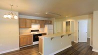 Located at 701 Juniper St in Foley, Alabama, this single-story home offers a practical and welcoming layout designed for comfortable everyday living. The kitchen serves as a central feature of the space, boasting warm honey-toned wood cabinetry that provides generous storage throughout. A peninsula-style breakfast bar with decorative corbel supports extends into the living area, creating a natural gathering spot and seamlessly connecting the kitchen to the rest of the home. White appliances, including a refrigerator and an electric range with a built-in ventilation hood, complement the light countertops and contribute to the kitchen's clean, functional aesthetic. Recessed lighting and a ceiling-mounted light fixture ensure the space is well-lit. Rich, dark hardwood-style flooring runs throughout, adding warmth and contrast to the neutral wall tones. A built-in shelving unit is visible through an adjacent doorway, offering additional storage and organizational flexibility. The overall ambiance is bright, clean, and move-in ready, making this single-floor property a solid option for those seeking a comfortable home in the Foley, Alabama area.