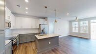 Located at 4115 Dr. Martin Luther King Jr. Blvd in New Bern, NC, this single-floor, 2-bedroom, 2-bathroom residence offers a thoughtfully designed layout with modern finishes throughout. The open-concept kitchen and living area serves as the heart of the home, anchored by a granite-topped center island with a built-in sink and stylish pendant lighting. Two-tone cabinetry — white upper cabinets paired with gray lower cabinets — complements the stainless steel appliances and tile backsplash. Rich hardwood-style flooring extends across the main living areas, adding warmth and continuity. The living room is bright and airy, with multiple windows fitted with blinds and a ceiling fan, and offers direct access to a private balcony. Both bedrooms feature plush carpeting, ceiling fans, and ample natural light. The spacious primary bedroom includes generous closet space with built-in wire shelving. The bathrooms are finished with granite-topped vanities, gray cabinetry, and wood-look flooring, with one featuring a full tub-shower combination. A dedicated in-unit laundry room with washer and dryer hookups adds everyday convenience, completing this well-rounded and move-in ready home.