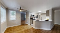 Located in Bellevue, WA, this well-appointed 3-bedroom, 2-bathroom residence offers a thoughtfully designed single-floor layout with generous living space. The open-concept living, dining, and kitchen area serves as the heart of the home, featuring warm hardwood-style flooring, crown molding, and a classic white-mantled fireplace that anchors the living room. Large sliding glass doors lead to a private balcony, filling the space with natural light and providing outdoor views. The modern kitchen is outfitted with stainless steel appliances, sleek flat-front cabinetry in a warm wood-tone finish, a white quartz peninsula countertop, and a ceiling-mounted light fixture. A ceiling fan adds comfort to the connected living area. The three bedrooms offer a mix of hardwood-style and plush carpeted flooring, with generous closet space throughout — including walk-in closets — and windows with blinds providing privacy and natural light. The bathrooms are clean and contemporary, featuring wood-tone vanities with white countertops and full tub-shower combinations. With seven closets total, storage is abundant throughout this well-organized and comfortable Bellevue residence.