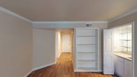 This single-floor residence offers a practical and well-organized layout across several distinct living areas. The main living space features rich hardwood-style flooring, crown molding, and a textured ceiling, with large multi-pane windows and a glass door that invite generous natural light. A built-in white bookcase adds both character and storage to the living area, which connects to an entryway leading to the front door.

The galley-style kitchen is efficiently designed with ample white cabinetry extending to the ceiling on both sides, light stone-look countertops, a double stainless steel sink, and black appliances including a refrigerator, electric range, and microwave. A closet is conveniently accessible from within the kitchen.

The bedrooms are carpeted and each equipped with ceiling fans and natural light from blinds-fitted windows. One bedroom features a dedicated vanity area with a wide mirror, stone-look countertop, white cabinetry, and a spacious walk-in closet with open shelving.

The bathrooms include a full tub-shower combination with white square tile surround and chrome fixtures, maintaining a clean, bright aesthetic throughout. Consistent neutral tones and hardwood-style flooring in common areas lend the space a cohesive, move-in-ready feel.