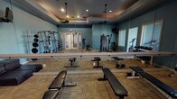 Located at 1501 Westpark View Dr in Fort Worth, Texas, this fitness center offers a comprehensive, single-floor workout facility designed to accommodate a wide range of exercise needs. The space is divided into distinct functional zones, each thoughtfully appointed with quality equipment and a cohesive aesthetic featuring teal-toned walls, warm carpet tile flooring, and elevated tray ceilings with recessed lighting that lend the space a polished, modern feel.

The primary workout area is anchored by a full wall of floor-to-ceiling mirrors, enhancing the sense of openness while allowing users to monitor their form during training. Multiple adjustable weight benches, a multi-station cable machine, a weight rack loaded with plates, and a dumbbell rack covering a broad range of weights provide ample options for strength training. A medicine ball rack and additional functional fitness equipment round out the free-weight section.

A dedicated cardio zone, bathed in natural light from large floor-to-ceiling windows, offers outdoor views of the surrounding community and houses several treadmills and elliptical machines. A ceiling fan overhead ensures comfort during use. Additional equipment, including a back extension bench and cable pull-down machine, is distributed throughout the space. French-style glass doors provide easy entry and exit, completing this well-organized and inviting fitness facility.