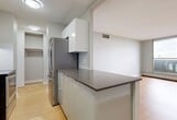 Located at 10127 121 Street NW in Edmonton, Alberta, this one-bedroom, one-bathroom unit offers a thoughtfully laid-out single-floor plan with a clean, modern aesthetic throughout. Light hardwood flooring flows seamlessly across the living room, bedroom, and kitchen areas, lending warmth and visual continuity to the space.

The open kitchen is designed in a galley style, featuring sleek white cabinetry with ample upper and lower storage, grey laminate countertops, a white tile backsplash, and stainless steel appliances including a refrigerator, stove, and dishwasher. A peninsula counter extends into the living area, providing additional workspace and a natural separation between cooking and living zones.

The living room is bright and open, with light grey walls and windows that frame outdoor views, filling the space with natural light. The bedroom is generously sized, offering a built-in sliding-door closet with shelving and hanging space, along with a window overlooking the surrounding cityscape. Baseboard heating is present throughout the living and bedroom areas.

The bathroom is finished in a clean, neutral palette with white subway-style wall tiles, light grey floor tiles, a full soaker tub with shower, and a modern vanity with a white countertop. A dedicated closet provides additional storage within the unit.